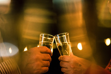 close up of two hands with glass with champagne clinking together to celebrate the new year or something party alones
