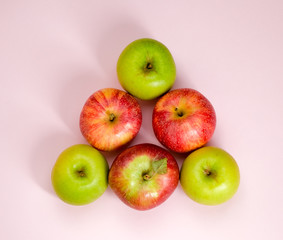 Ripe juicy apples of new crop. Group of colorful apples in a shape of triangle isolated on pink background. Symbol of healthy lifestyle. Fruits rich in vitamins, iron. Harvest festival, organic food. 