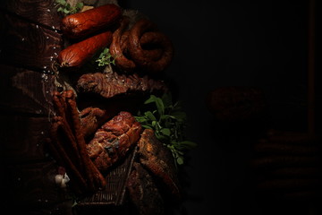 Sausage on a dark background. Composition of sausages and hams on a wooden countertop.