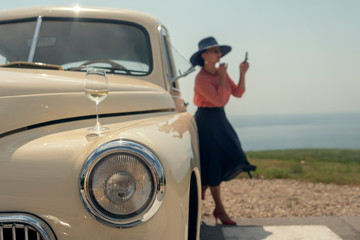 A woman in a hat adjusts makeup at a vintage car. Travel, vacation