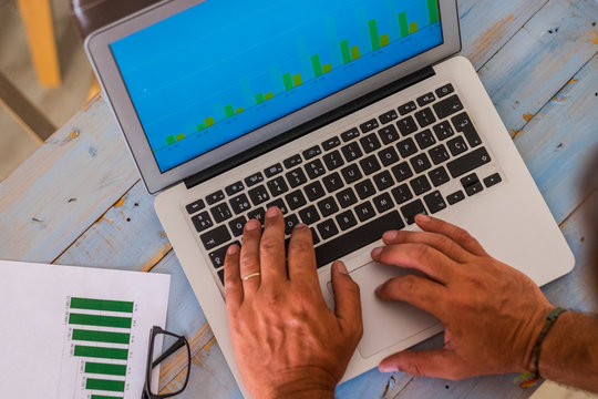 close up of hands writing and working with laptop at the office on a blue wood table with stadistics and graphs