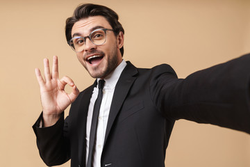 Image of joyful businessman showing ok sign while taking selfie photo