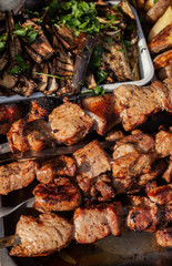 Roasted meat on a skew is on the table next to fried potatoes and vegetables in the open air