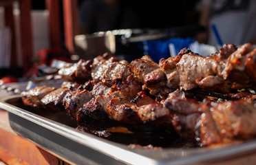 Roasted meat on a skew is on the table next to fried potatoes and vegetables in the open air