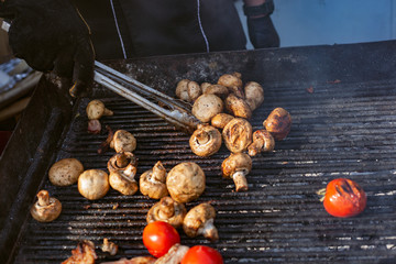 brazier in a black tunic grills meat and vegetables by turning them over with iron tongs