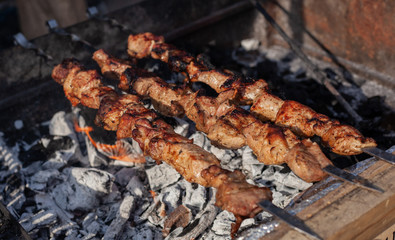 Meat on a skewer is fried on hot charcoal on an iron barbecue.