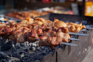 Meat on a skewer is fried on hot charcoal on an iron barbecue.