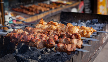 Meat on a skewer is fried on hot charcoal on an iron barbecue.
