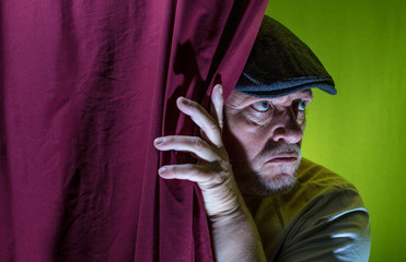 An elderly man looks secretly from behind a curtain. Concept: curiosity and espionage