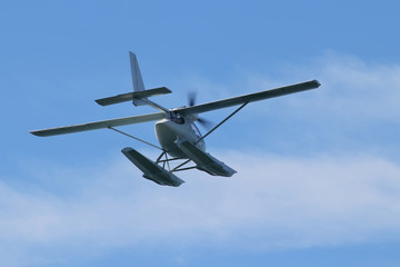 Floatplane (hydroplane or seaplane) flying in blue sky. Cabin, wings propeller, engine, tail of plane are visible in details.