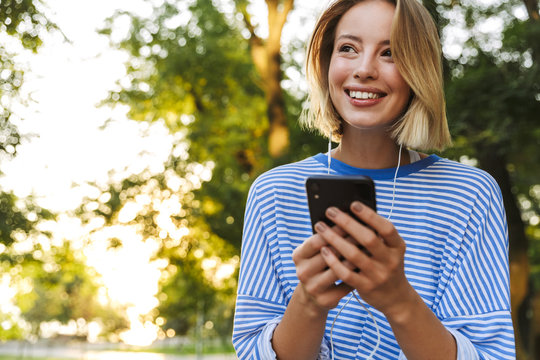 Image of blonde joyful woman using cellphone and earphones