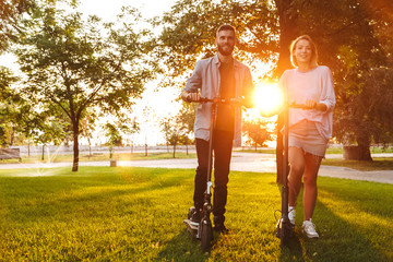 Image of caucasian joyful couple smiling while riding e-scooters