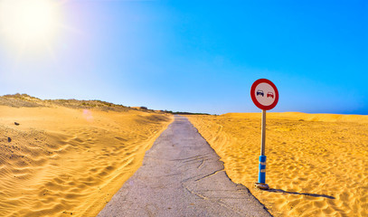 Cracked asphalt road crossing an arid dune terrain.