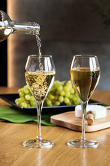 Pouring white wine into the glass above the table set with grape cheese appetizers