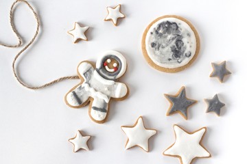 gingerbread man cookie in cosmonaut costume on white background with moon and stars
