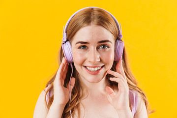 Fototapeta premium Happy girl isolated over yellow wall background listening music with earphones.