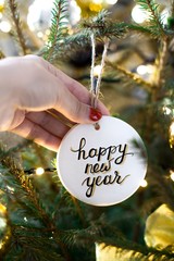 young woman holding christmas tree white ornament with happy new year sign on it