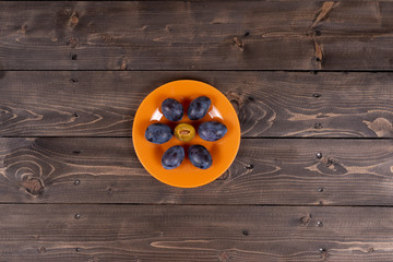 Plums on an orange plate on a wooden vintage table top view