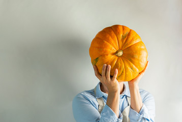 A woman in light clothes holds a large ripe pumpkin instead of a head. Food concept joke.