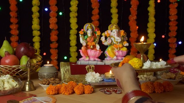 Indian female praying in front of Ganesh Ji and Laxmi Ji with a Puja thali on Diwali. Hands of a female worshipping Lord Ganesha and Goddess Lakshmi with a decorated festive background - Hindu Cust...