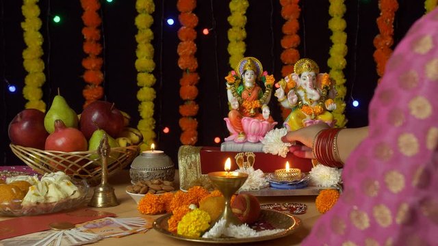 Over the shoulder shot of an Indian female praying in front of Ganesh Ji and Laxmi Ji - Diwali Puja. A young female is performing rituals of offering flowers in the temple of Hindu gods Lord Ganesh...