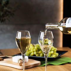 Pouring white wine into the glass above the table set with grape cheese appetizers