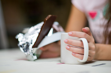 girl holds a mug of tea and chocolate bar on a table, close-up without a face