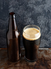 Beer bottle and a full glass of craft beer porter on a dark table