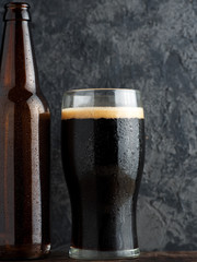 Beer bottle and a full glass of craft beer porter on a dark table
