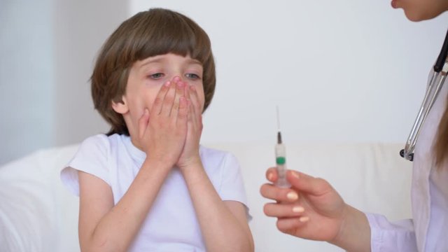 Portrait of child cute little boy afraid of injection. Doctor nurse pediatrician with medicine syringe in hand, protest against care, kid afraid and crying, treatment. Baby boy fear injection, 4 K