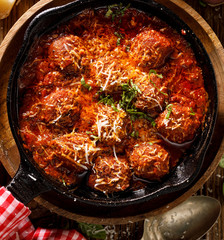 Meatballs in a tomato-herb sauce, sprinkled with parmesan cheese and chopped fresh basil served in a cast iron skillet, close-up, top view.