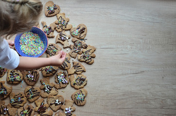 Little girl decorates handmade christmas cookies in different form on the wooden background with copy space. 