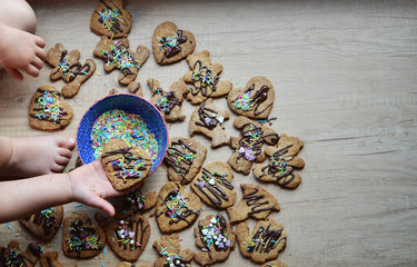 Little hand hold gingerbread heart and makes a decoration on the christmas cookies  in different shapes on the wooden table . Top view with copy space.