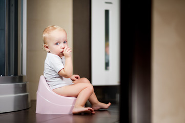 little girl sits on a pink pot in the bathroom and looks in surprise