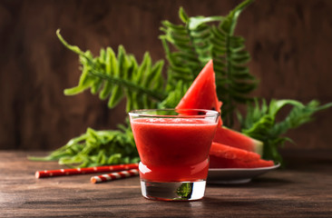Freshly squeezed watermelon smoothie in glass and slices of watermelon on old wooden kitchen table background