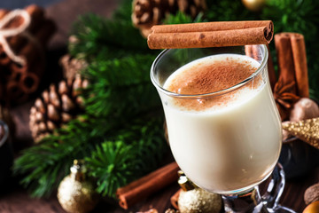 New Year or Christmas Eggnog cocktail - hot winter or autumn drink with milk, eggs and dark rum, sprinkled with cinnamon and nutmeg in a glass on wooden background, festive decoration