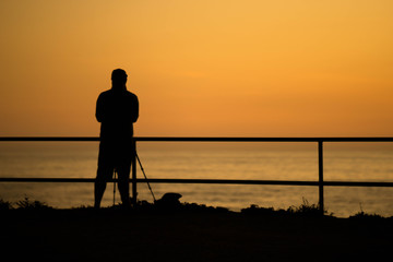 silhouette of a man setting up a camera during sunset by the ocean