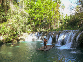 Lovely travel couple at the tropical wild nature adventure on the bamboo raft in Cambugahay Waterfalls in Siquijor Island, Philippines 