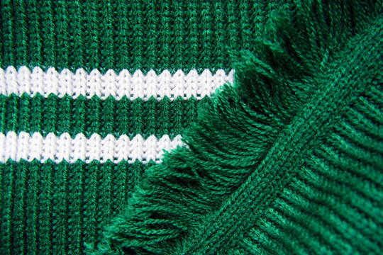 Knitted texture of green warm scarf with white stripes and fringe. Slytherin scarf, knitted background
