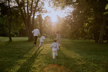 Little cute boys in stylish suits running after their mother and father trying to catch them , they are in the middle of a green park