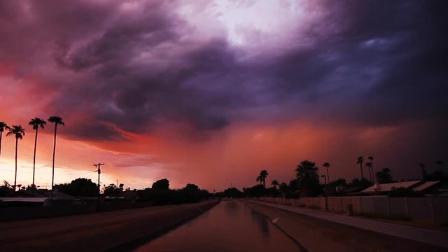 Sunset view of a canal and bike path on what could turn into a stormy night. There is a flash of lightening on the right and insect flies through the scene. A bird flies partway through at the end.