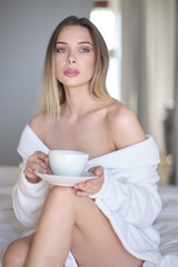 woman in a bathrobe drinks morning coffee in bed