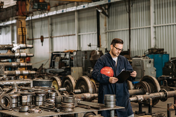 Manual worker looking at clipboard at train factory workshop.