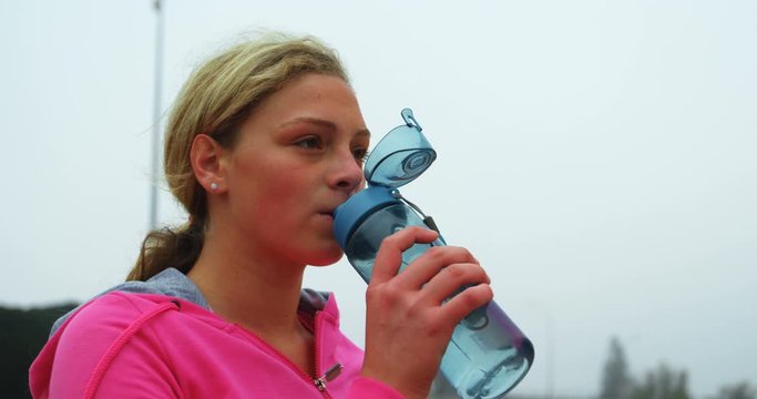 Front view of young Caucasian female athlete drinking water at sports venue 4k