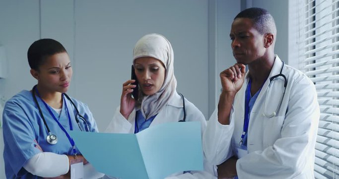 Front view of Middle-East female doctor talking on mobile phone with her colleagues in hospital