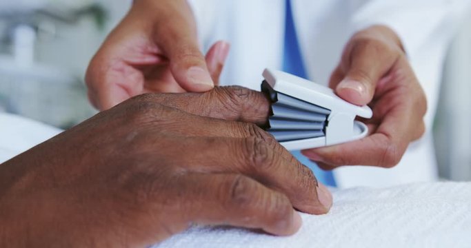 Close-up of African american female doctor attaching pulse oximetry on male patient hand in the ward