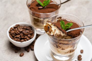 Portion of Classic tiramisu dessert in a glass cup on concrete background