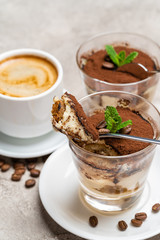 Portion of Classic tiramisu dessert in a glass and cup of coffee on concrete background