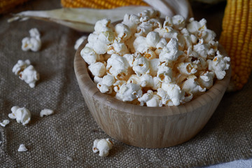 Traditional popcorn in a wooden bowl and corncobs on the table.