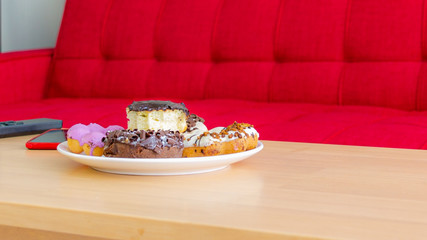 Donuts in dish on wooden table infront of red sofa, unhealty junk food